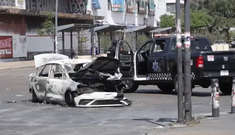 A Mexican military convoy with armored vehicles and armed soldiers parked on a highway with smoke in the distance.