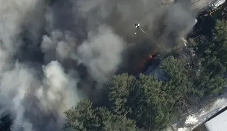 An aerial view of a large industrial building with a partially collapsed roof and black smoke rising into the air.